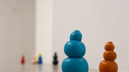 A dozen or so colorful Kongs on a concrete floor. A blue and brown one are the focal point in the foreground, with others blurred in the background.