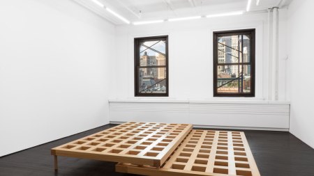 View of a small gallery showing a sculpture of two latticed wood elements that nestle on top of each other.