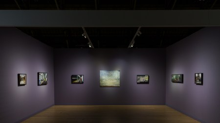 An art fair booth with purple walls and several paintings of New York City-scapes on the wall.