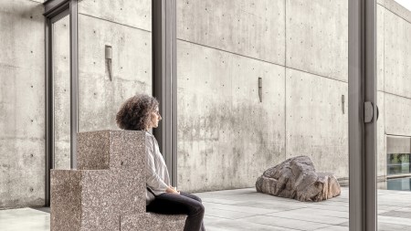 A woman sitting on a granite structure, peering out a window.