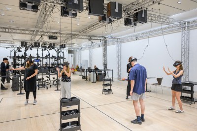 People standing in a space with squares of tape on its floor wearing headsets.