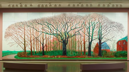 View of a 50-panel painting showing a set of trees in the countryside with two red barns on the right.