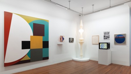 Artworks in a gallery on white walls, including a large geometric abstract painting.