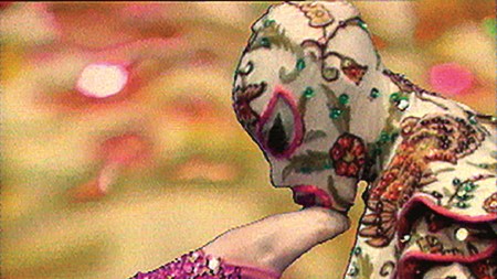 A hooded figure kissing the foot of another figure wearing spangly pink tights.