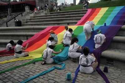 A group of people working together to knit a long Pride flag that spills down a staircase.