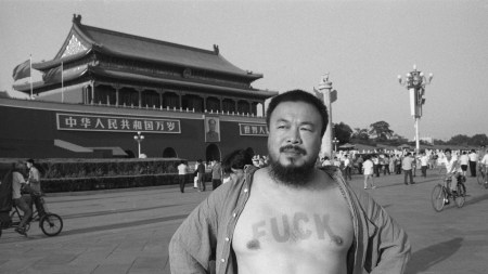 A bearded Chinese man stands in front of a traditional building with the word "fuck" sunburnt on his chest.