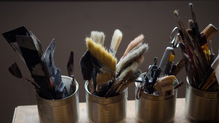 Brushes, pencils and other drawing tools are collected in three jars on the table in the artist's studio