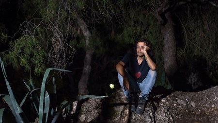 A photo of sculptor Adrián Villar Rojas sitting on a rock.