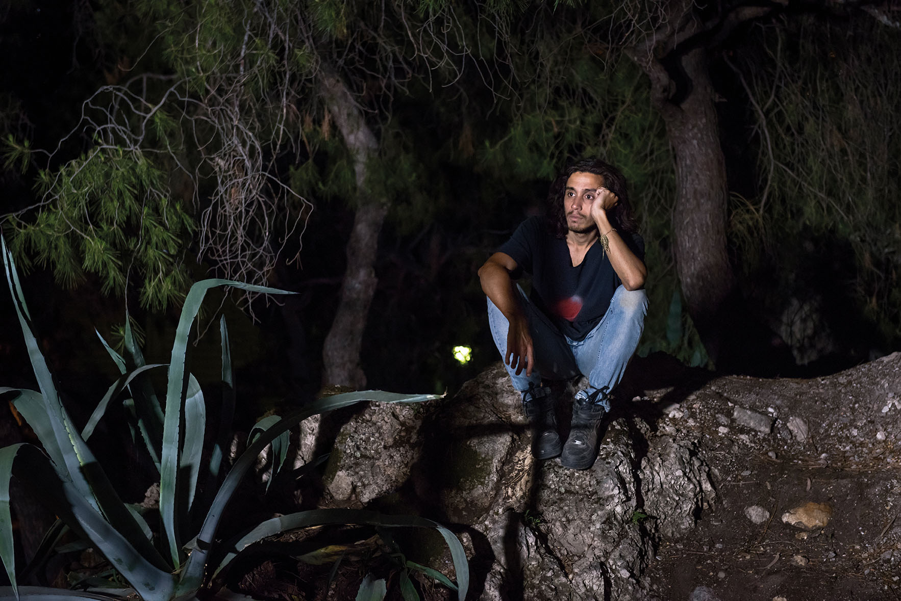 A photo of sculptor Adrián Villar Rojas sitting on a rock.