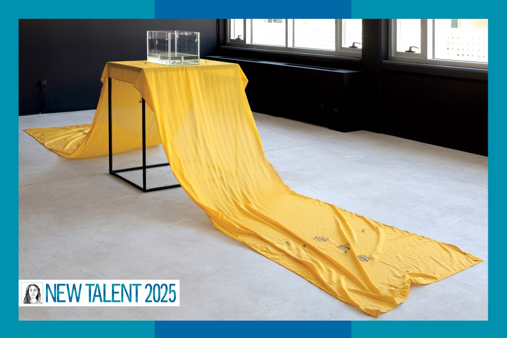 A long yellow sheet of fabric draped over a table, with a clear case of liquid on top.
