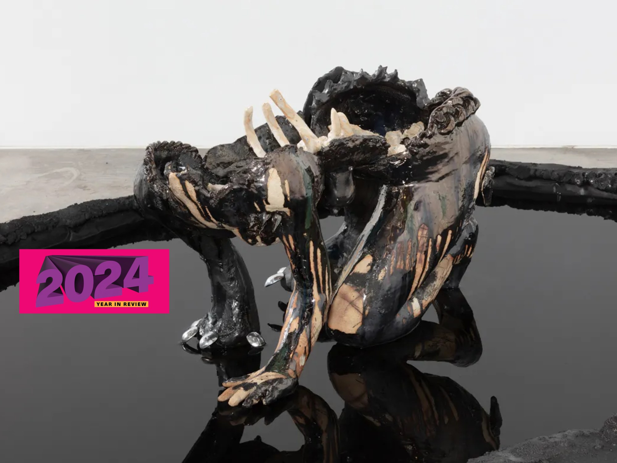 A humanoid sculpture without a head sits in a pool of motor oil.