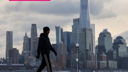 A man walks on snow in front of the New York skyline.