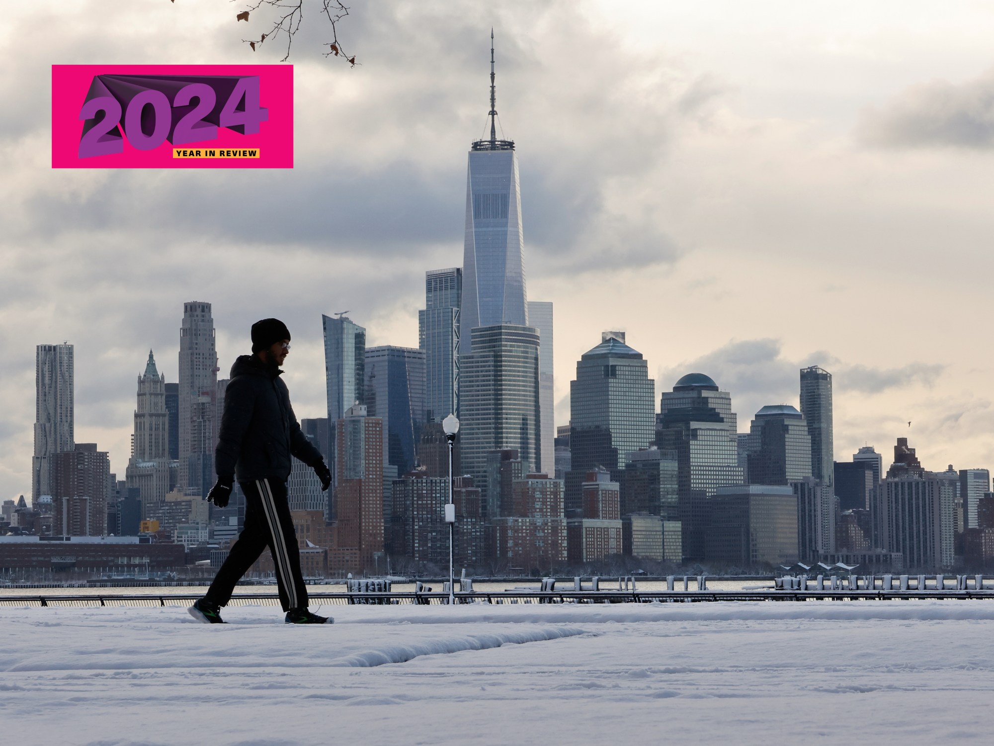 A man walks on snow in front of the New York skyline.