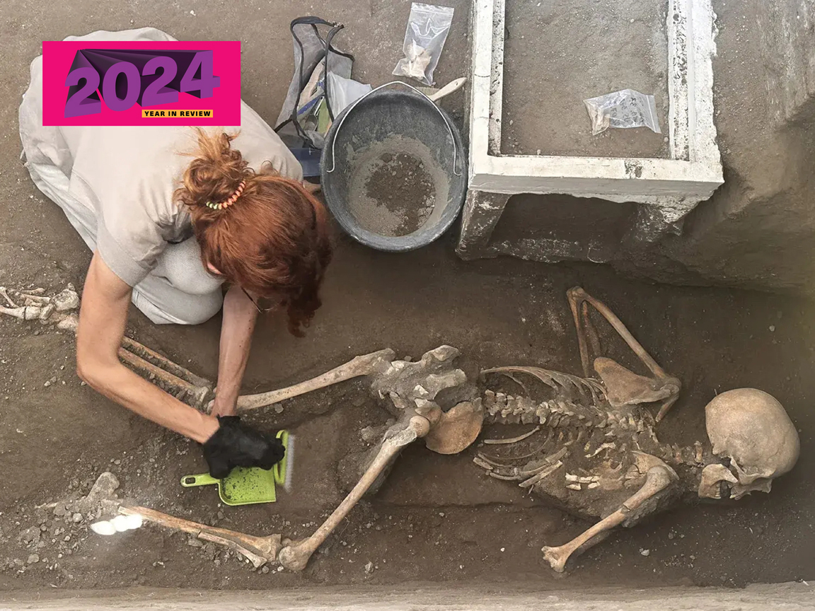 A female archaeologist carefully removes dust from a victim at Pompeii using a brush and dustpan.