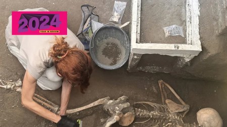 A female archaeologist carefully removes dust from a victim at Pompeii using a brush and dustpan.