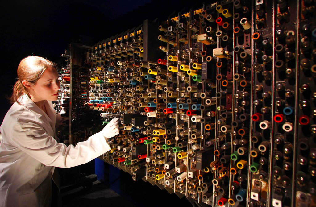 A woman in a white jacket touches one of many coils on a machine resembling a large grid.