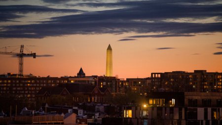 With the sun glowing over the horizon, many buildings (and a crane) are scene in a vast, dense city.