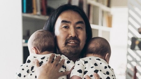 A Japanese man with long hair holds twin babies.