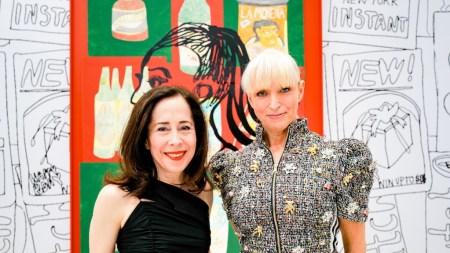 Two women stand in front or a big colorful print.