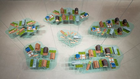 Six translucent islands of architectural miniatures resembling suburban developments dangle from a gallery ceiling.