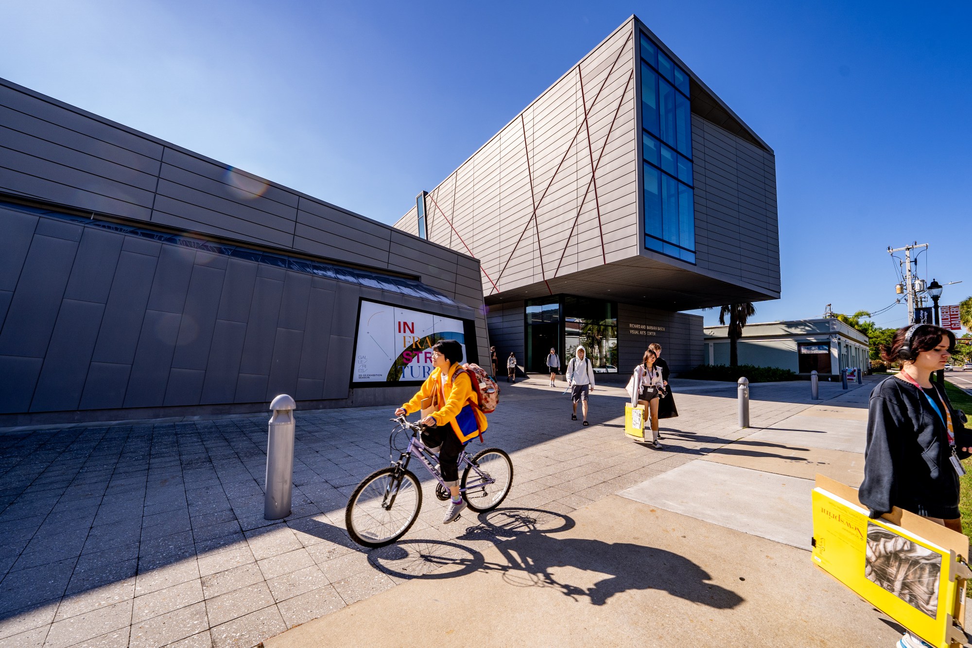 A student in a yellow jacket rides a bike in front of a building at the campus of Ringling College Art and Design, a private arts school in Sarasota, Florida. Ringling recently started offering a certificate in AI for its students. 