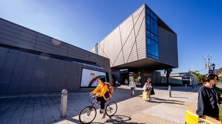 A student in a yellow jacket rides a bike in front of a building at the campus of Ringling College Art and Design, a private arts school in Sarasota, Florida. Ringling recently started offering a certificate in AI for its students.
