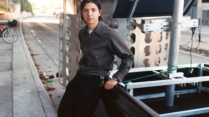 Portrait of Carlos Agredano leaning against a pickup truck near a freeway overpass.