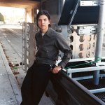 Portrait of Carlos Agredano leaning against a pickup truck near a freeway overpass.