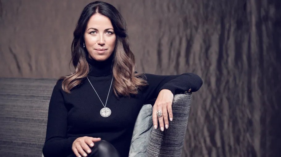 A woman in a black turtleneck looks at the camera.