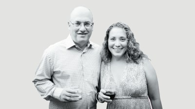 Black-and-white portrait of a middle-age white couple who are holding glasses in their hands.