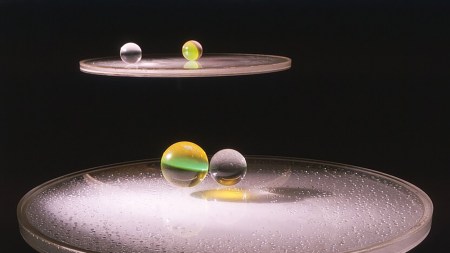 Two clear discs filled with condensation hover in a black void. There are a pair of clear marbles placed atop eatch disc.