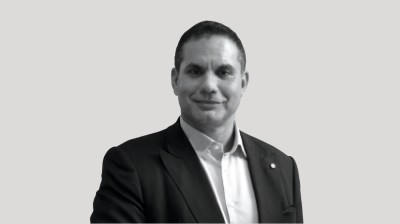 A silhouetted black-and-white portrait of an Egyptian man in a suit on a gray background.