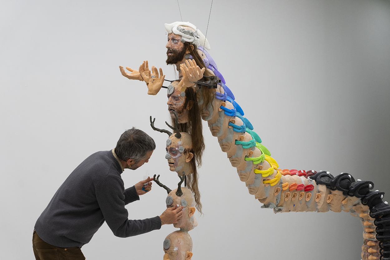 A white man is arranging a stack of sculpted heads.