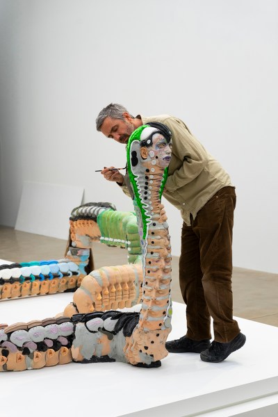 A white man is painting the lime green head of a snake sculpture that is almost as tall as he is.