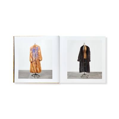 A book spread with each page showing fur coats on mannequins. The back of one coat is covered in purple paint.
