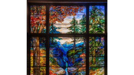 A monumental stained glass window showing a nature scene of a forrest, stream, and mountain the background.