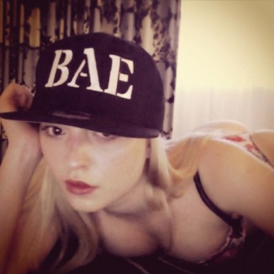 A blonde girl wearing a big hat that says BAE in a grainy picture with an instagram filter.