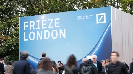 Fairgoers walk in front of the sign for Frieze London.