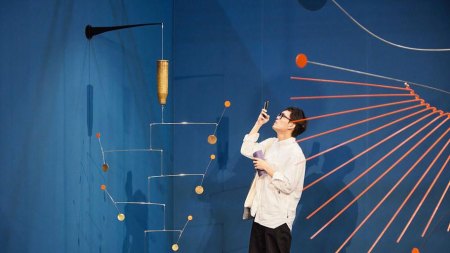 A man takes a photo of a sculpture resembling a mobile.