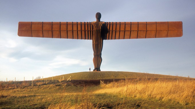 A monumental sculpture of an angel spreading its wings above a field.