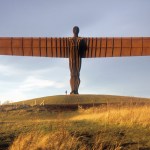 A monumental sculpture of an angel spreading its wings above a field.