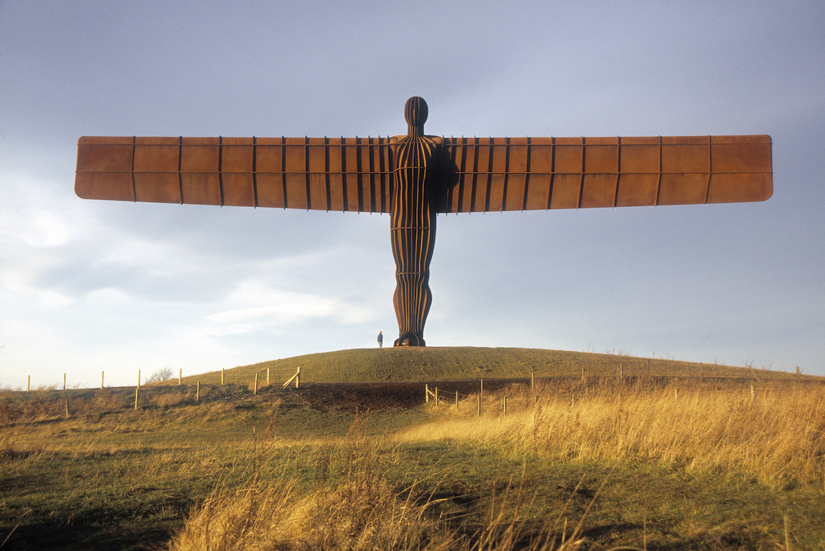 A monumental sculpture of an angel spreading its wings above a field.