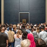 A crowd of people before a painting.