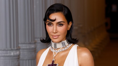 A smiling woman in a white dress wearing a cross-shaped necklace.