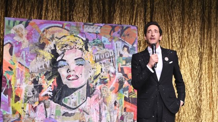 A man in a tuxedo beside a painting of Marilyn Monroe collaged with various materials.