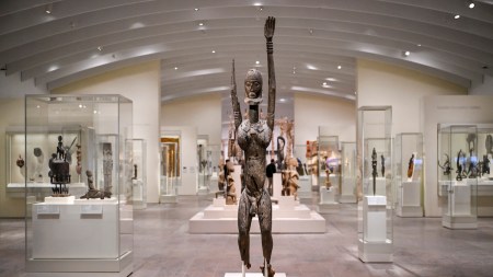 A sculpture of a person with one extended hand before many other display cases.
