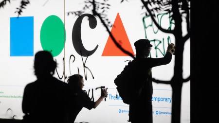 Protestors spray-painting phrases on a sign reading 'MOCA.'