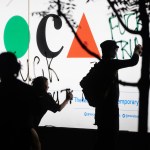 Protestors spray-painting phrases on a sign reading 'MOCA.'