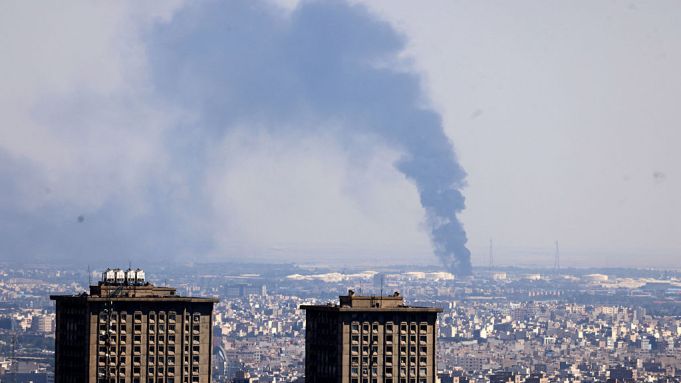 TOPSHOT - Smoke billows in the distance from an oil refinery following an Israeli strike on the Iranian capital Tehran on June 17, 2025. Israel and Iran exchanged fire again, the fifth day of strikes in their most intense confrontation in history, fuelling fears of a drawn-out conflict that could engulf the Middle East. (Photo by ATTA KENARE / AFP) (Photo by ATTA KENARE/AFP via Getty Images)