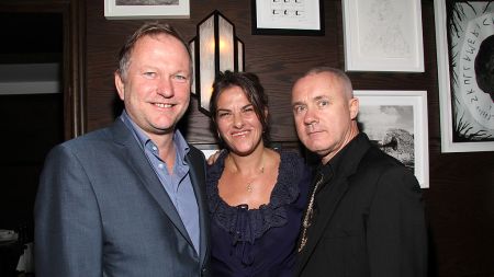 Two men stand each side of a smiling woman.